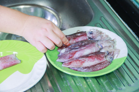 Hand arranging fresh squid with empty plate beside