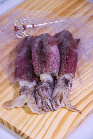 Three Squids on Wooden Cutting Board with Partial Net, Vertical Arrangement