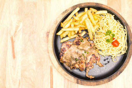 Pork steak and fries and spaghetti on a plate placed on a wooden table.の写真素材