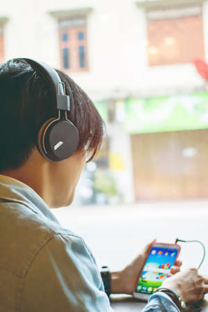 Teenagers Man wearing headphones sitting on the phone with light Sunset.の写真素材