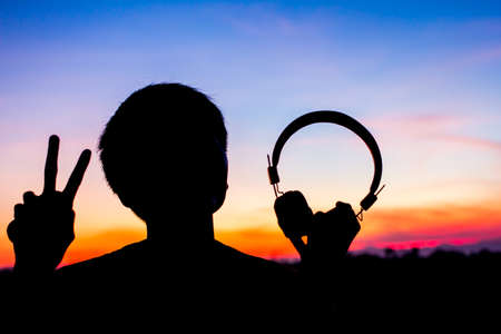The headphones and holding two fingers Silhouette sunset blur for background.の写真素材