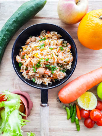 Fried rice sausage and eggs in the pan is lemon, tomatoes, cucumbers, peppers and carrot lettuce on the wood.の写真素材