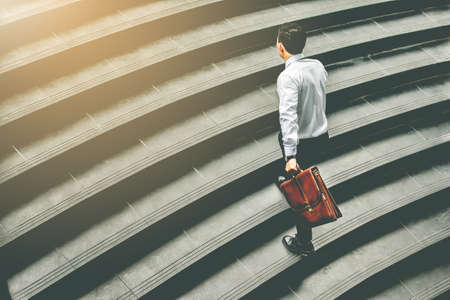 Young Asian businessman holding Brown leather bag  working on  staircase go office hurry work time with sunset top view and vintage toneの写真素材