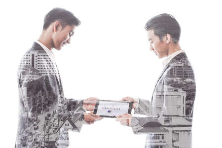 Double exposure. Two Asian people  young businessman are smiling and using tablet presenting graph of work with cityscapeの写真素材