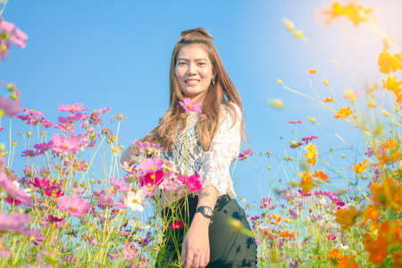 Focus flower.Portrait,Asian Beautiful girl smiling standing in cosmos flower garden with sunset light , park outdoor.の写真素材