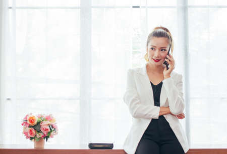 Asian business woman  with long hair smiling .Holding black smart phone,Talking cosmetics and clothing online shopping at coffee shopの写真素材