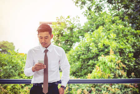 Asian young businessman holding mobile phone chat meetings the commercial processes involved in promoting and selling and distributing a product or serviceの写真素材