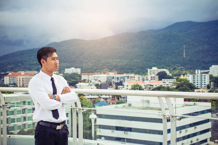 Young asian businessman in white shirt cross one's arm standing on terrace .View landscapes and...