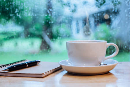 White cup hot coffee on table wooden and window with raindrop. Copy space for your text. Vintage tone. Soft Focus blurの写真素材