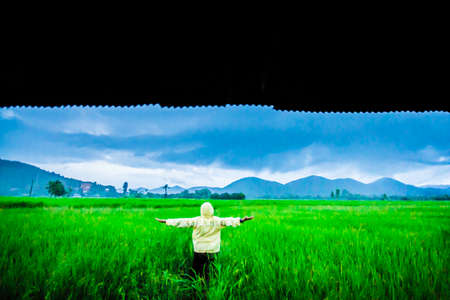 Grain, Noise, Soft Focus.One man in  long Sleeve Yellow Shirt standing arms, freedom  in the green field looking mountain Rain dayの写真素材