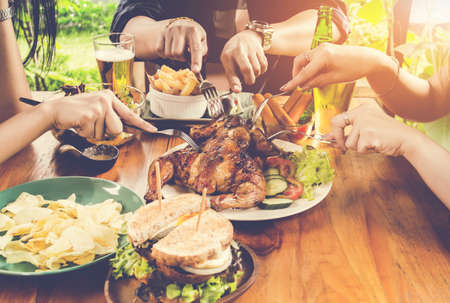 Close up hand, eating.Group Of People Dining Concept,With  Chicken roasting,salad,French fries on wooden tableの写真素材