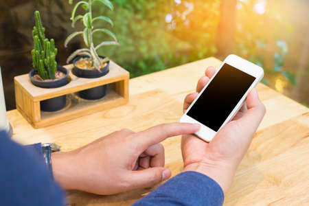 Close up of men  hands holding touching mobile phone with blank copy space for your text message in cafe with light Sunset,Vintage tone.Selective focusの写真素材
