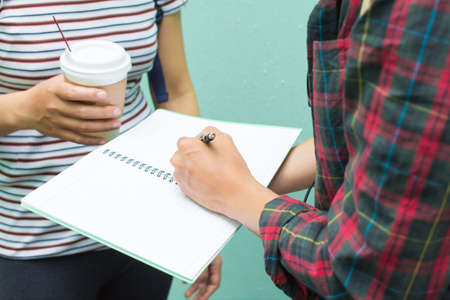 Education concept. Two Asian women one student or roommate with friend helps analyzing workbook learning outdoor , Tutor books with friends.On green background.Selective focusの写真素材