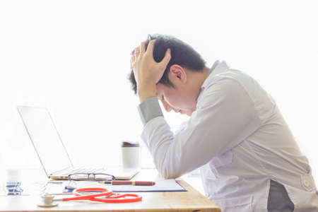 Stressed, Asian Doctor in sitting at his desk  with Headphones in his office at the hospitalの写真素材