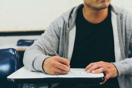Close up , male with beard , holding pencil exams writing in classroom for education test ,Copy space for your text.Vintage tone with sunset light ,Education concept.の写真素材