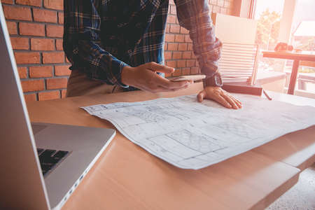 Concept architects, asian man engineer holding phone between executives pointing equipment architects On the desk with a blueprint in the office, Vintage, Sunset light.Selective Focusの写真素材