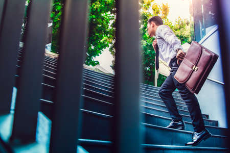 Young Asian businessman holding Brown leather bag working on staircase go office hurry work time with sunset top view and filter photo vintage toneの写真素材