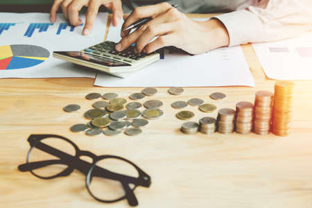 Business man or accountant in gray shirt holding pen working on accounts and using  calculator and writing on desk, With sunset light.の写真素材