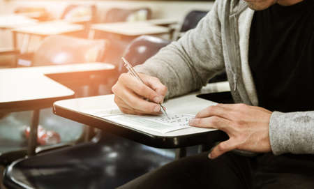 Student holding pencil writing on paper answer sheet.sitting on chair doing final exam attending in examination on classroom.の写真素材
