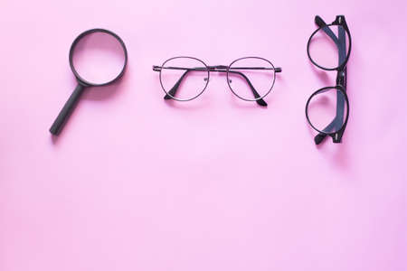 Glasses and magnifying glass on black . Minimal style layout Leave blank for the text. On a pastel pink backgroundの写真素材