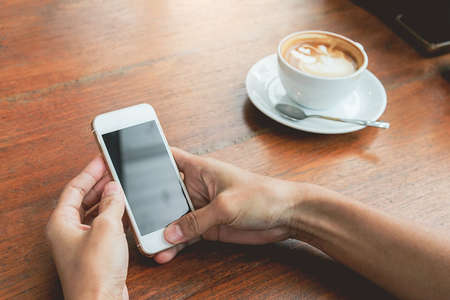 Close up of woman hands holding touching mobile phone with blank copy space for your text message in cafe with light Sunset,Vintage tone.Selective focusの写真素材