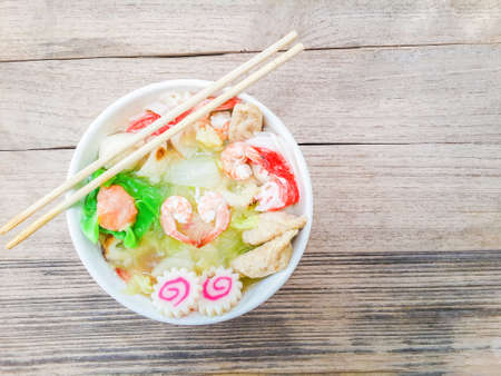 Sukiyaki or shabu soup with Dumplings, white cabbage, crab, vermicelli, shrimp, and chopsticks in a white cup on woodenの写真素材
