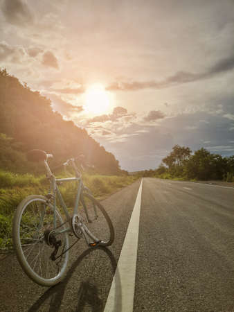 Green vintage bicycle on the road with sunset background.