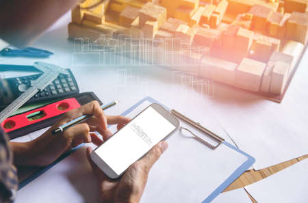 Concept architects,Using digital smartphone shooting, architect hands making model building, house. On the desk with a blueprint in the office, Vintage, Sunset light.Selective Focusの写真素材