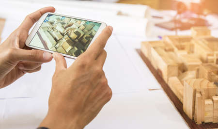 Concept architects,Using digital smartphone shooting, architect hands making model building, house. On the desk with a blueprint in the office, Vintage, Sunset light.Selective Focusの写真素材