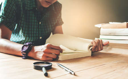 Man in green plaid shirt.Sitting on wood chair, reading book on table.の写真素材