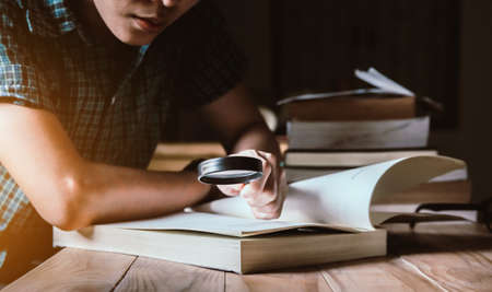 Man in green plaid shirt.Holding Magnifying glass.Sitting on wood chair, reading book on table.の写真素材
