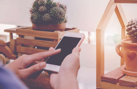Close up of  woman hands holding touching mobile phone with blank copy space for your text message in cafe with light Sunset,Vintage tone.Selective focusの写真素材