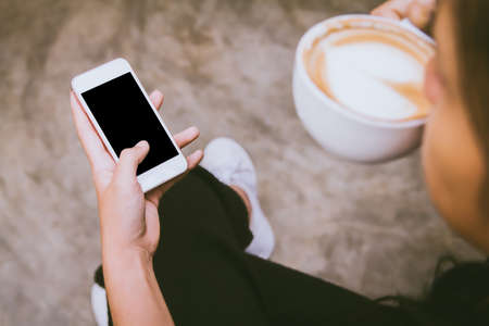 Close up of  woman drinking coffee hands holding touching mobile phone with blank copy space for your text message in cafe with light Sunset,Vintage tone.Selective focusの写真素材