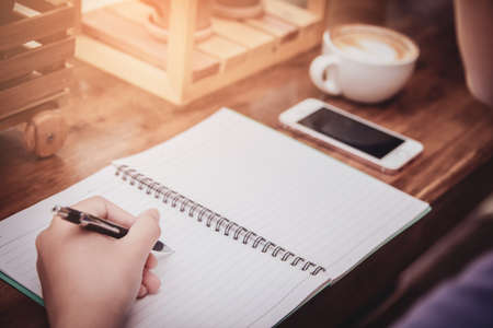 Close-up cup of hot coffee. Asian young women in plaid shirt holding pen writing a tax report