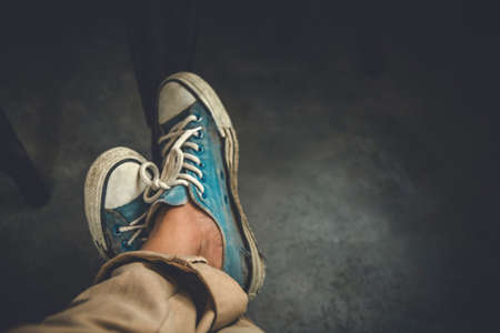 Man wearing old blue sneakers in brown trousers sitting on coffee shop,Vintage tone.Selective focusの写真素材