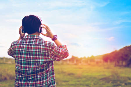 Man in plaid shirt are listening to music at close range with a light sunset background.の写真素材