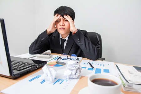 Asian young man in black suit are stress worry probleme working sitting on chair in office.の写真素材