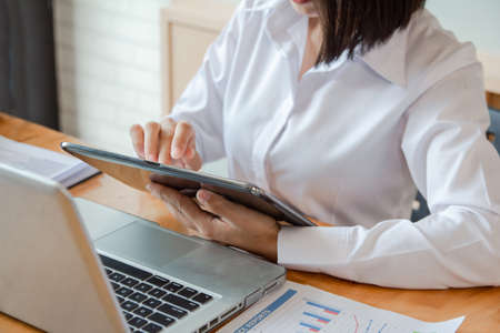 Business woman using tablet pointing to discuss the graph up and down of economy in office.の写真素材