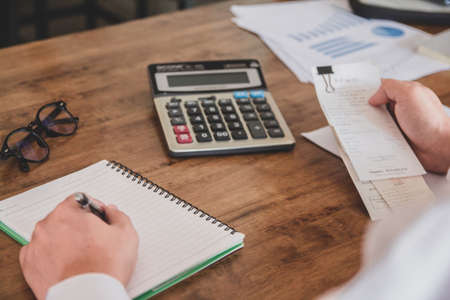 Asian young man in white shirt holding pen working ,Calculate tax lead to liquidation, With Sunset light vintage style.の写真素材