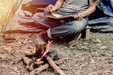 Asian young man sitting is reading a book in outside the tent. Alone camping in forest.の写真素材