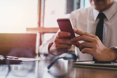 Business man of hands holding touching mobile phone with blank copy space for your text message in cafe with light Sunset,Vintage tone.Selective focusの写真素材