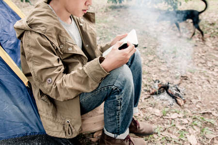 Asian young man sitting is reading a book in outside the tent. Alone camping in forest.