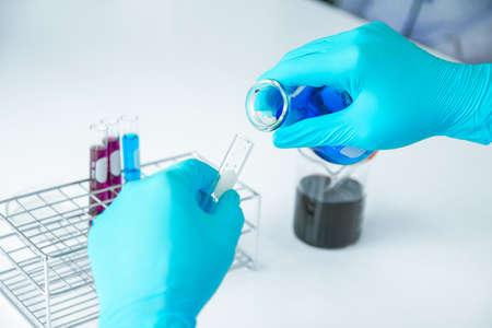 Medical science or male in laboratory room researcher performs tests with blue liquid pouring...
