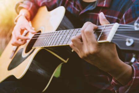 Close-up hand of Man in tartan shirt wearing headset and playing guitar of string song on gold rice field with sunset light evening.の写真素材