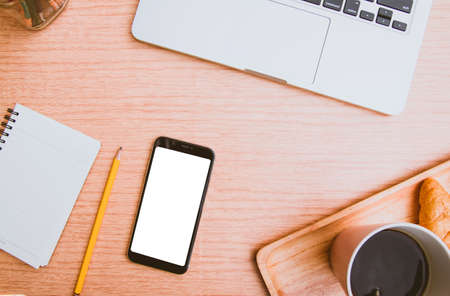 Mock up white screen on black mobile phone with note paper yellow pencil digital laptop and cup of coffee, croissant on wood. Filler vintage Pantone color trend for 2019 Year Top viewの写真素材