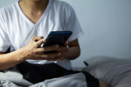 Young man sitting on the bed using smartphone at late night, Phone disease and Nomophobia. Healthy Conceptの写真素材