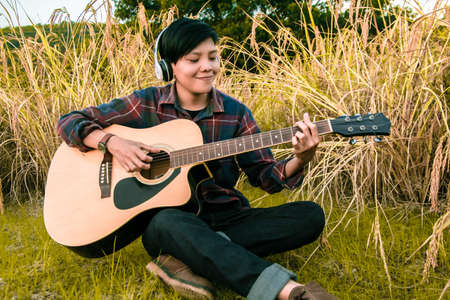 Man in tartan shirt wearing headset and playing guitar of string song on gold rice field in the...