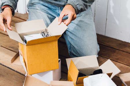 Asian young man Unpack the postal box,parcel while He was surprised and happy sitting on Wooden floor at homeの写真素材