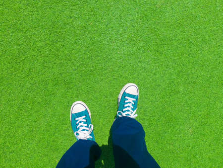 Man wearing old green sneakers in blue trousers standing on green grass outdoor.の写真素材