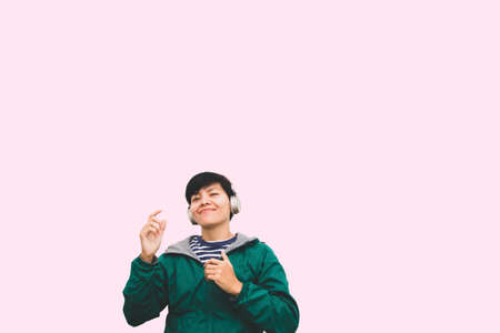 Asian handsome young man in green jacket wearing headset listening pop music and dancing are happy fun in headphones on pink pastel backgroundの写真素材